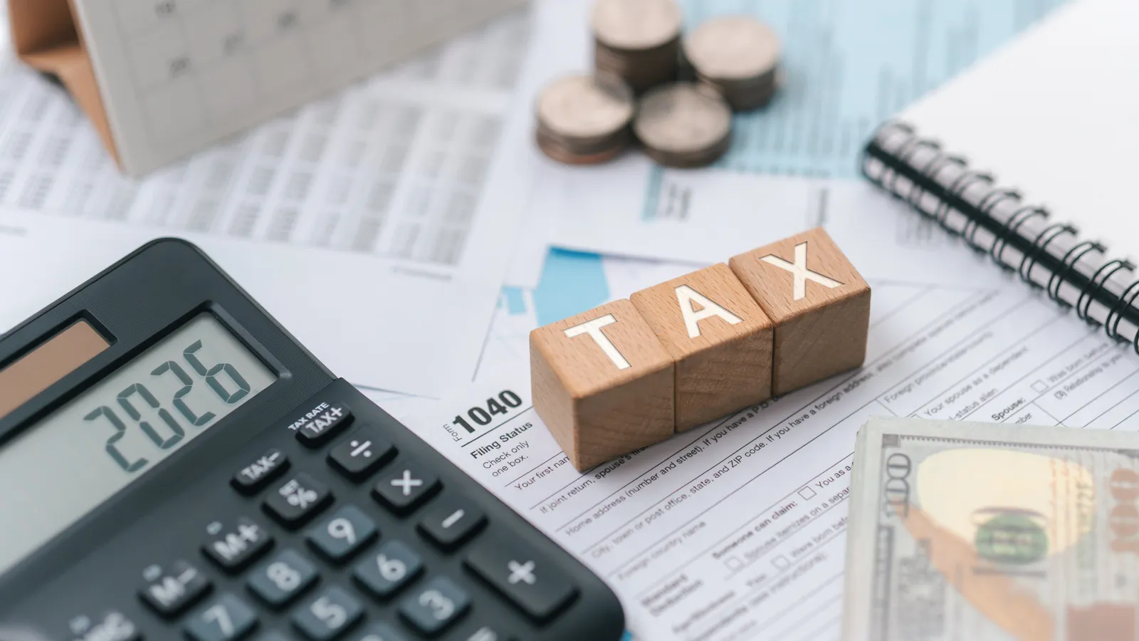 Calculator showing 2026 beside wooden blocks spelling TAX and tax forms